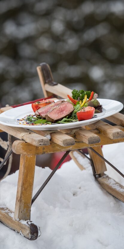 Teller mit Rindsteak und Gemüse auf Schlitten im Schnee | © Günther Pichler