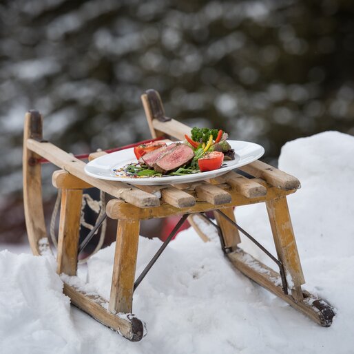 Piatto con bistecca di manzo e verdure su una slitta nella neve | © Günther Pichler