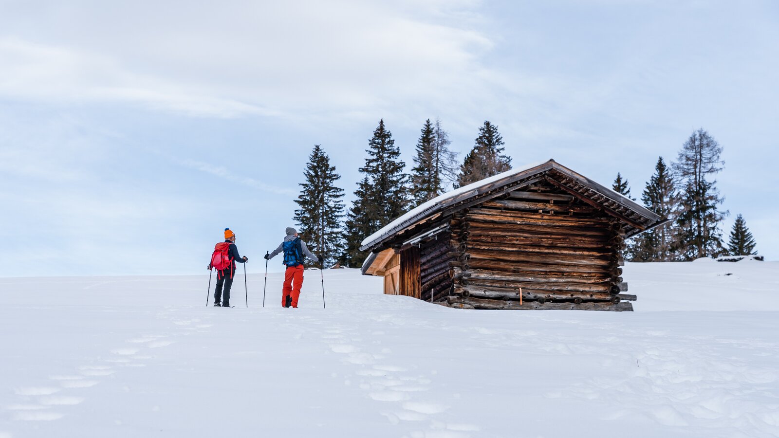 Schneeschuhwanderer auf Wiese mit traditioneller Almhütte | © Eggental Tourismus/Clicktext