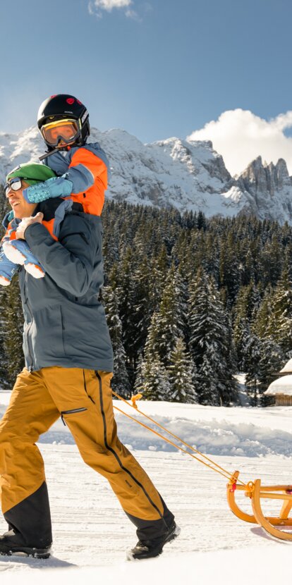 Padre e figlio in slitta vista Latemar | © Carezza Dolomites/StorytellerLabs